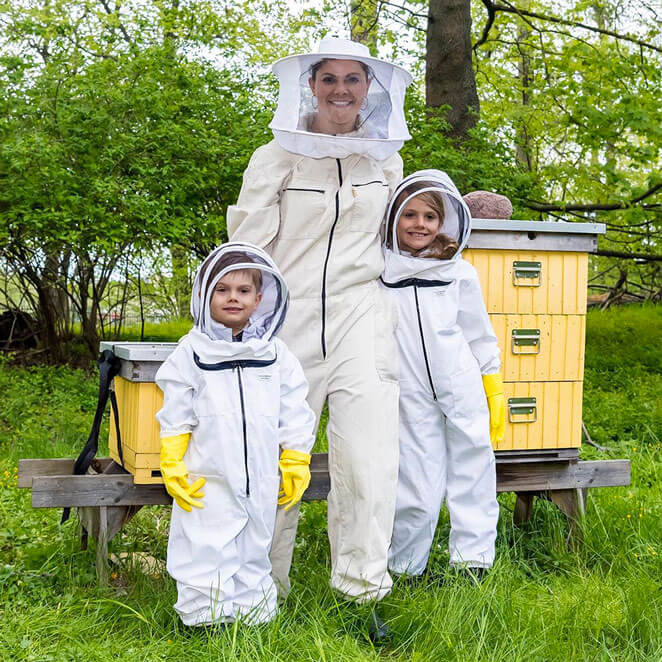 La princesse Viktoria de Suède et ses enfants le prince Oskar et la princesse Estelle, devant une ruche en tenue d'apculteur