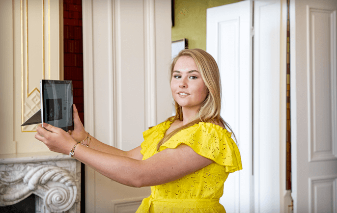 La princesse Amalia des Pays-Bas dans une robe jaune tenant un iPad