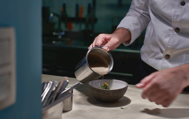 Gros plan sur les mains du chef du restaurant San Sablon Valerio Borriero verse une sauce dans un bol 