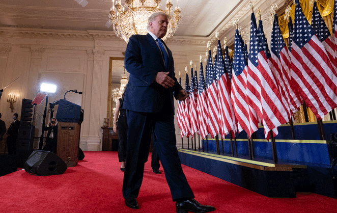 Donald Trump passe devant une rangée de drapeaux américains sur un tapis rouge